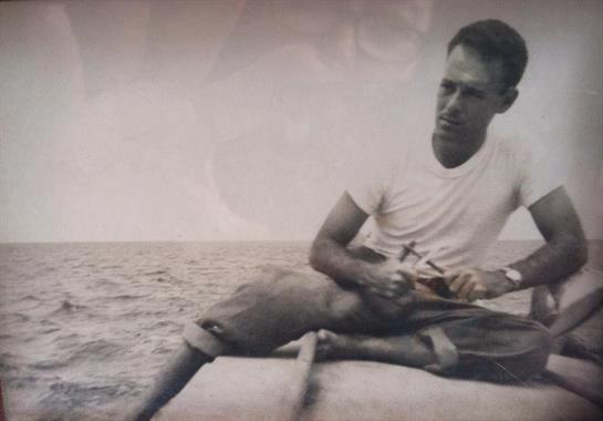 A man sits in a small boat rowing calmly across open water, focusing intently as the sun sets.
