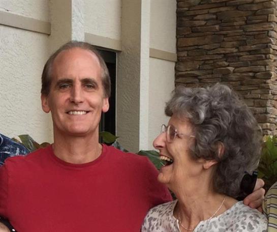 Two people share a heartfelt laugh outside, surrounded by a charming, rustic backdrop.