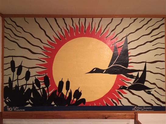 A colorful mural showcases birds in flight against a bright orange sun and reeds.