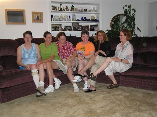 Seven friends sit comfortably on a couch in a cozy living room, sharing smiles and conversations.