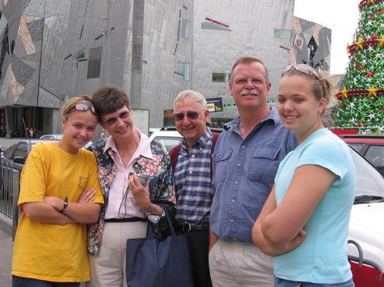 A cheerful group of five family members stands outside a contemporary structure, smiling together.