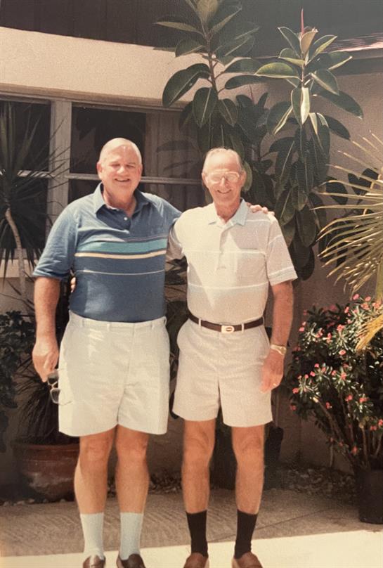 Two older men stand side by side in a bright garden, enjoying their time together.