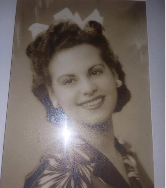 Woman smiles in a vintage portrait, showcasing her curly hair and floral-patterned outfit.