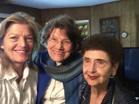 Three women are happily posing together, showcasing warm expressions and friendship indoors.
