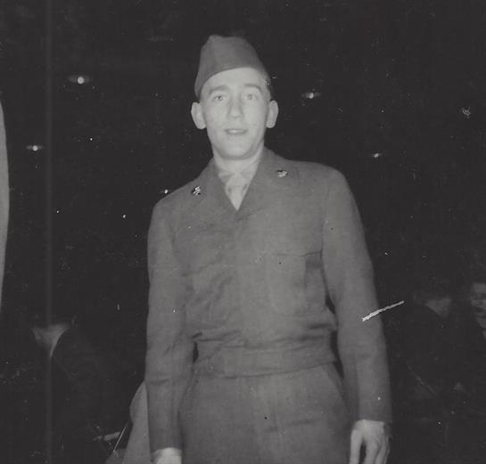 A young soldier in uniform proudly stands during a nighttime event, surrounded by onlookers.