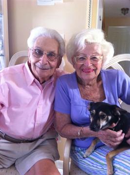 Couple smiles joyfully while sitting together, holding their pet dog in a warm, inviting room.
