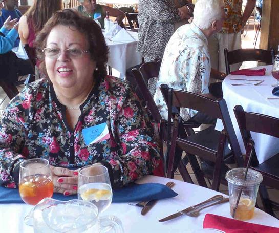 A cheerful woman seated at a table shares laughter and drinks with friends during a lively event.