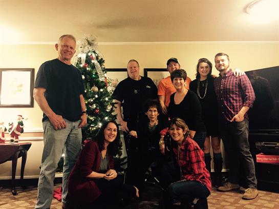Friends and family pose joyfully by a beautifully decorated Christmas tree in winter.