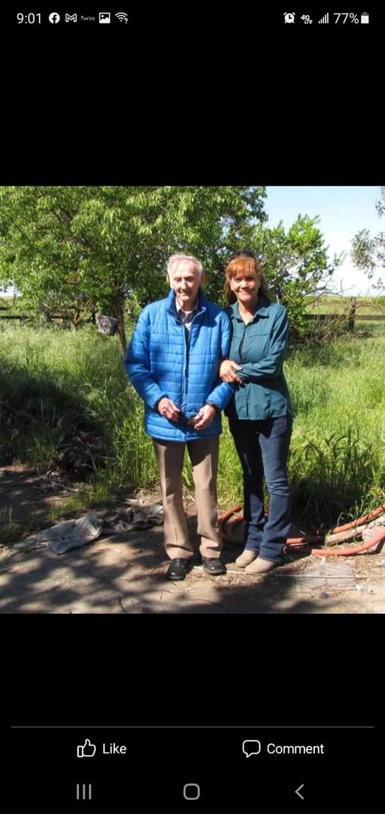 A man and a woman stand together smiling in a lush green field, enjoying a sunny day.