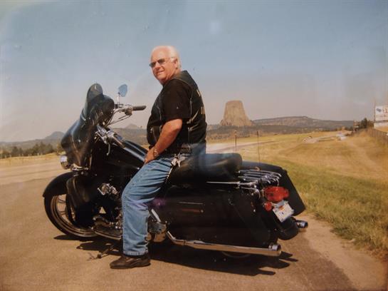 An older man sits on a motorcycle, enjoying the peaceful landscape with rocky formations.