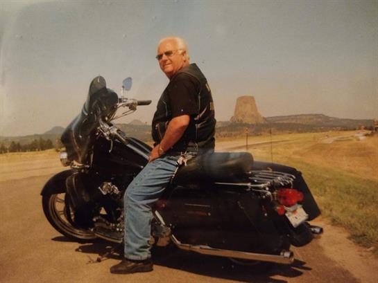 Man sits confidently on motorcycle, enjoying views of natural rock formations in the distance.