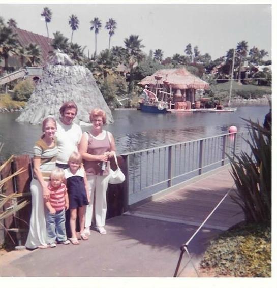 A family poses on a walkway by a waterway with attractions and palm trees in the background.