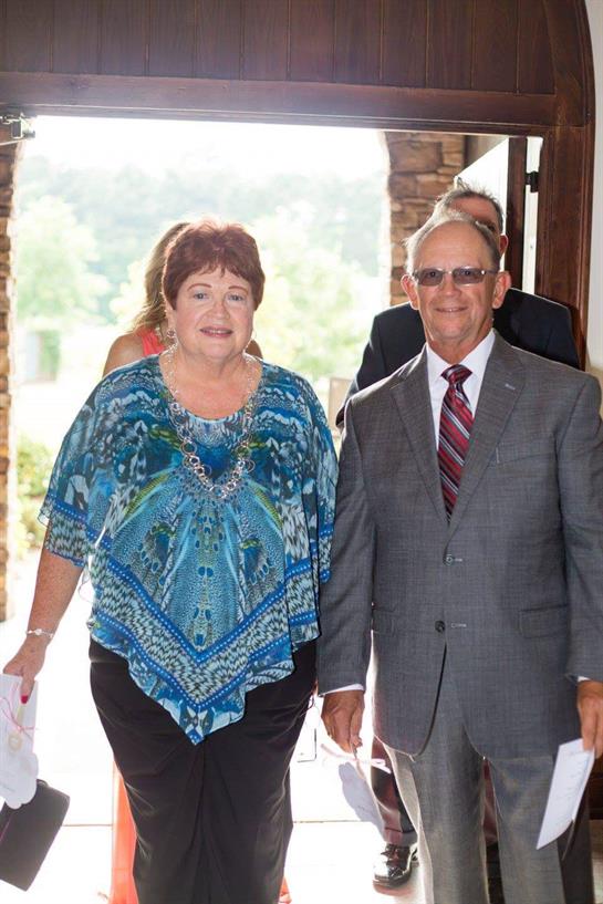 Two individuals walk joyfully outside a venue, dressed elegantly and enjoying a sunny day.