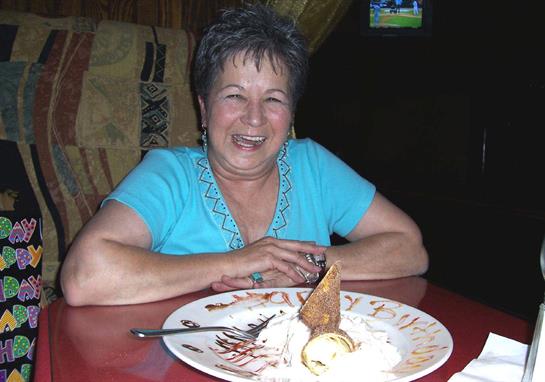 A cheerful woman with short hair smiles while sitting at a table, enjoying dessert after her meal.