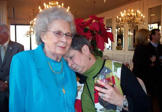 Two women embrace each other affectionately, surrounded by holiday decorations and joyful ambiance.