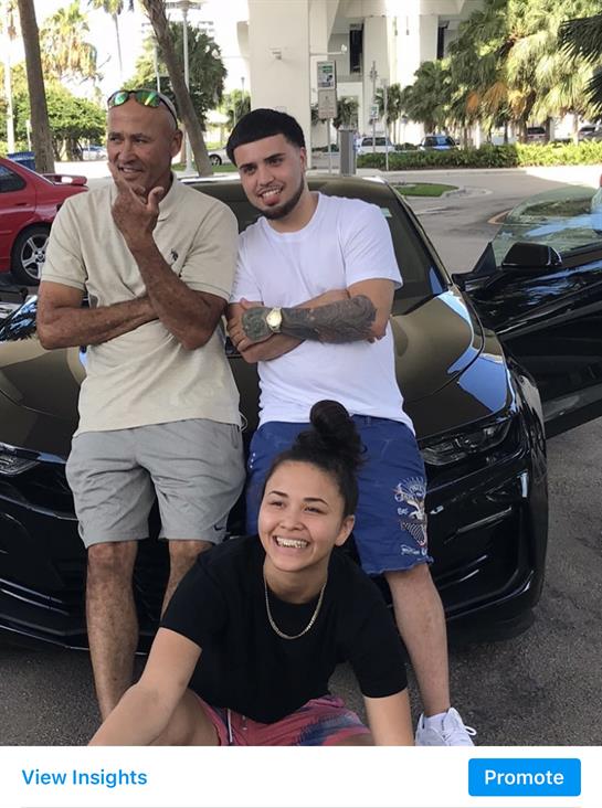 Three friends pose happily in front of a stylish car, enjoying a cheerful moment outdoors.