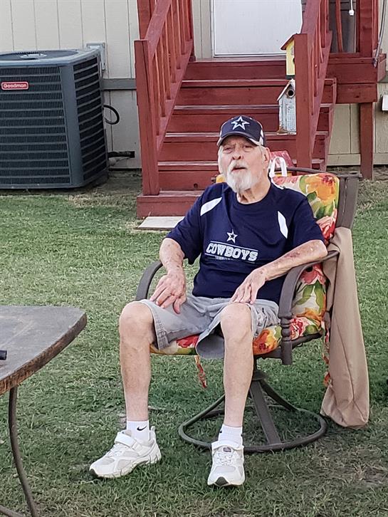 An elderly man enjoys some leisure time sitting in a vibrant chair on a sunny day outside a home.