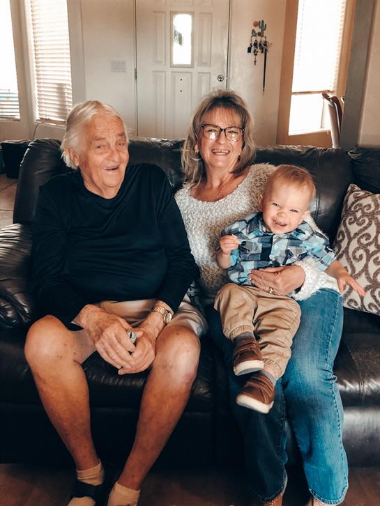 Grandparents enjoy a joyful moment with their smiling grandchild on a couch at home.