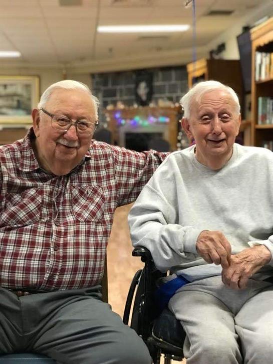 Two seniors share smiles and laughter together in a communal space.