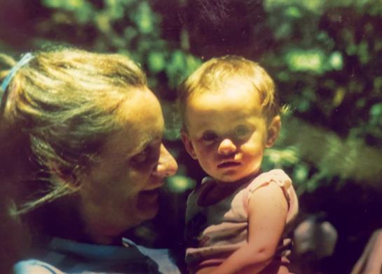 An elderly woman enjoys quality time with a toddler in a beautiful garden filled with greenery.