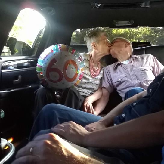 A couple joyfully kisses inside a car while celebrating their 60th anniversary with friends.