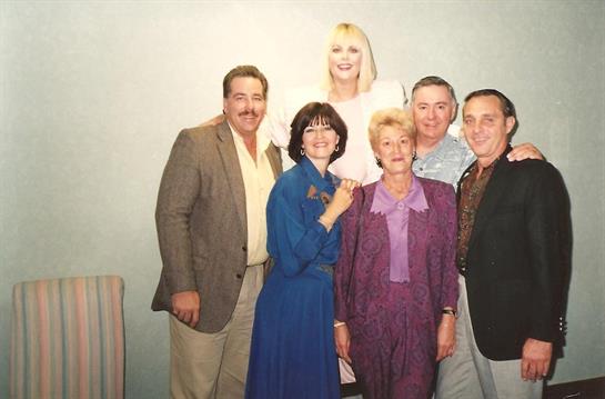 A diverse group of friends happily reunites in a casual indoor setting.