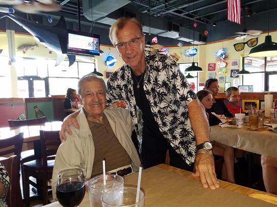 Two friends share a joyful moment at a restaurant, enjoying food and drinks in a lively atmosphere.