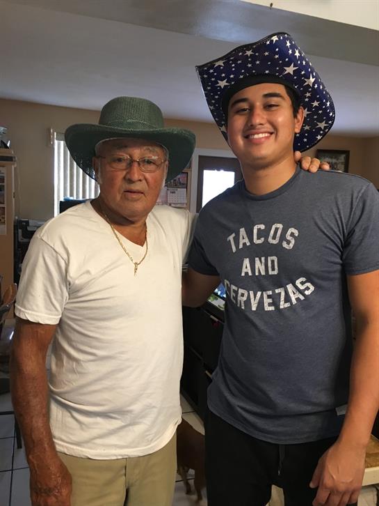 Two men stand together in a cozy living room, smiling proudly while wearing hats.