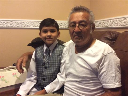 A boy in formal wear sits beside his smiling grandfather in a cozy room.