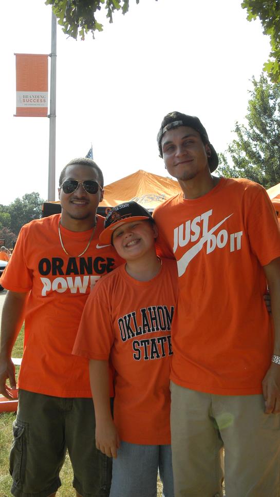 Three friends wear bright orange shirts, embodying school spirit at a lively outdoor event.