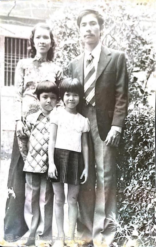 Two children pose in front of adults in a garden, dressed in vintage clothing from the 1970s.