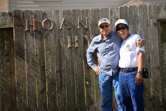 Two friends stand proudly at the Hoan Hy sign, enjoying a sunny day outdoors with smiles.