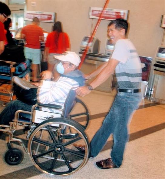 A man helps another person in a wheelchair navigate through a crowded airport.