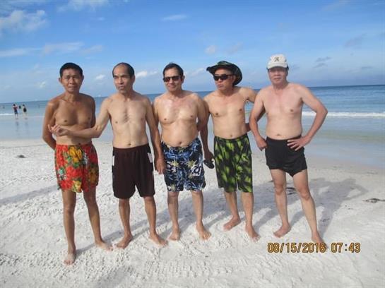 Five friends stand together on the beach, smiling and enjoying a sunny day by the water.