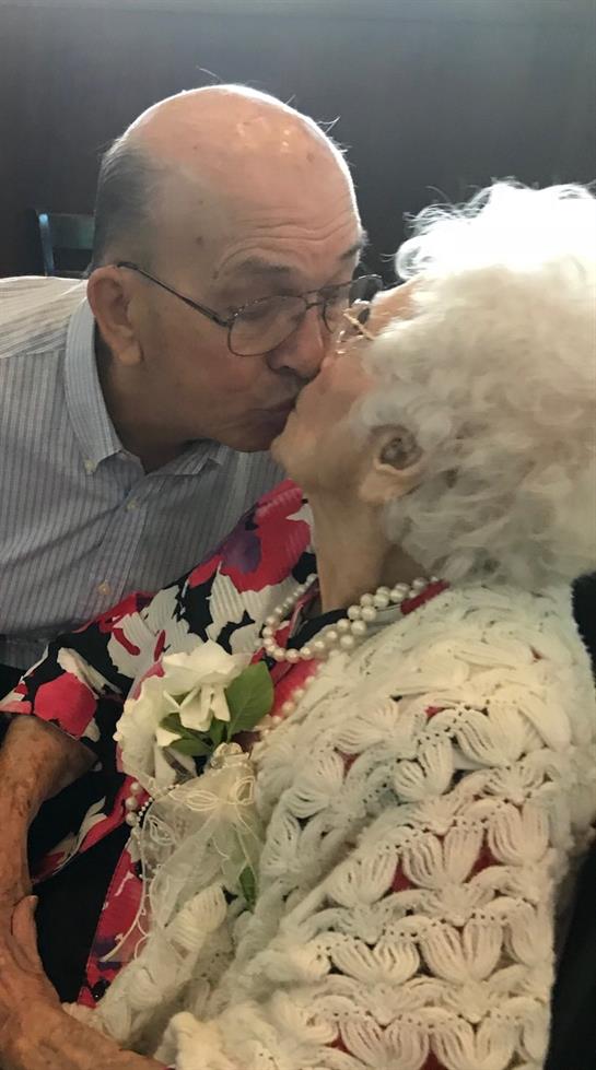 A joyful elderly couple embraces and kisses during a lively community celebration, radiating love.