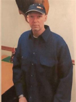 Individual stands confidently in a well-lit indoor space, wearing a blue shirt and hat.