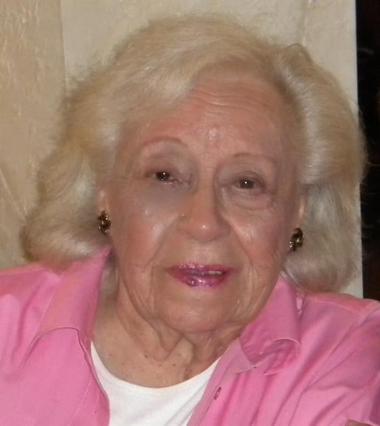 A stylish elderly woman with blonde hair smiles warmly in her cozy home.