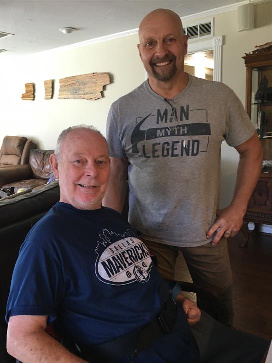 Two men share laughter and relax in a comfortable living room filled with warm light.