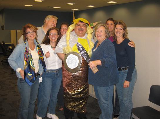 Colleagues gather with joy around a coworker dressed in a creative costume, celebrating teamwork.