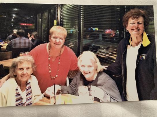 Four friends share laughter and food in a bustling restaurant filled with conversation.