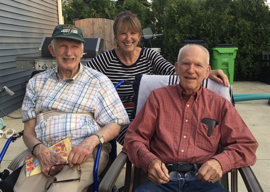 Three people enjoy a warm evening outdoors, sharing smiles and laughter while seated together.