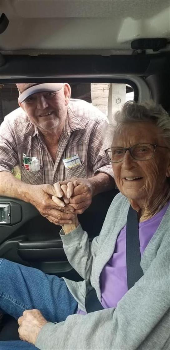 An elderly couple smiles joyfully, holding hands in a truck, sharing a sweet moment together.