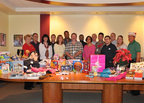 A diverse group gathers at a community center table displaying charity donations.