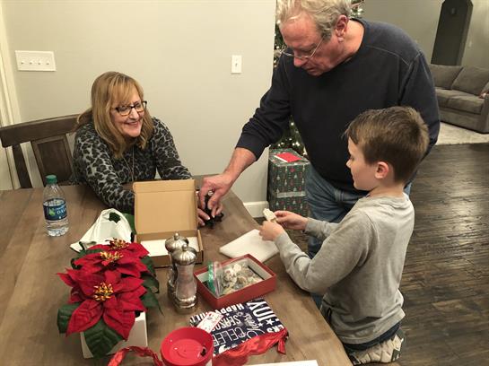 Adults and a child share smiles while opening presents during a family holiday gathering.
