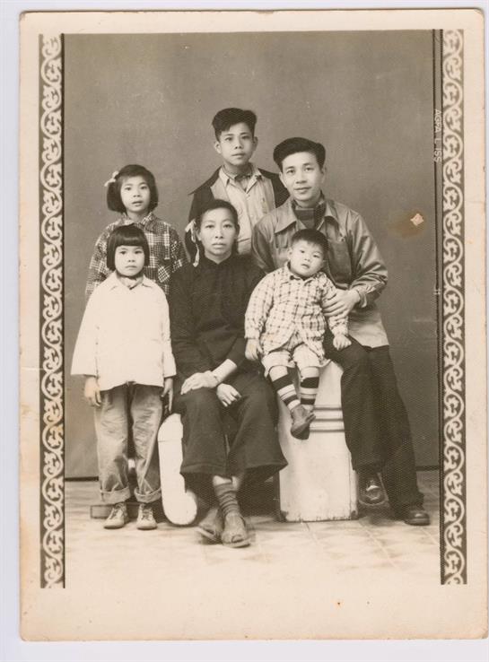 Four children and two young adults pose together in a classic studio, highlighting family ties.