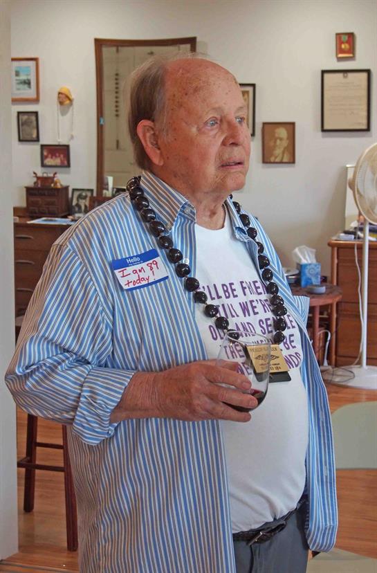 Man in casual attire holds a drink, surrounded by friends at a warm community event.