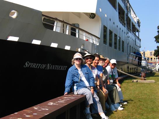 Friends pose on a railing by a cruise ship, enjoying a sunny day in a vibrant harbor setting.