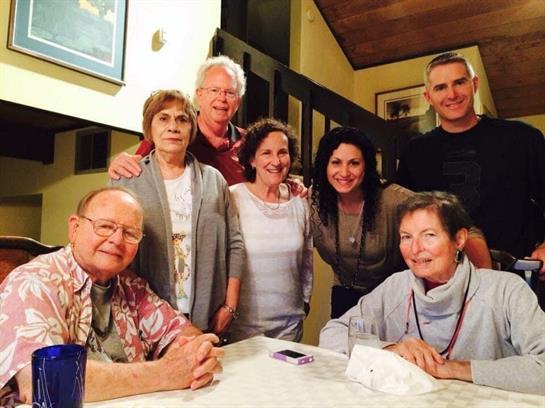 A group of eight friends shares laughter and conversation around a dining table at night.