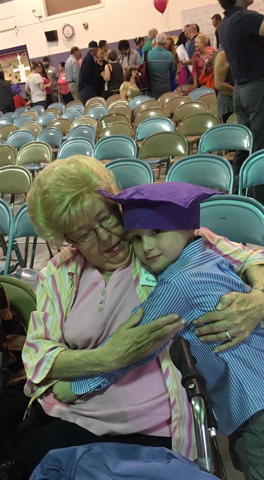 A grandmother holds her grandson who is wearing a graduation cap and smiling with joy.