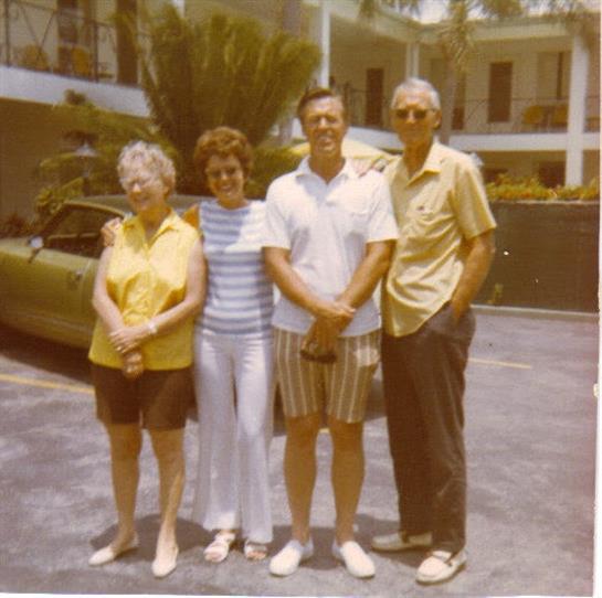 Four people stand together outside a residential complex, enjoying a sunny day and sharing memories.
